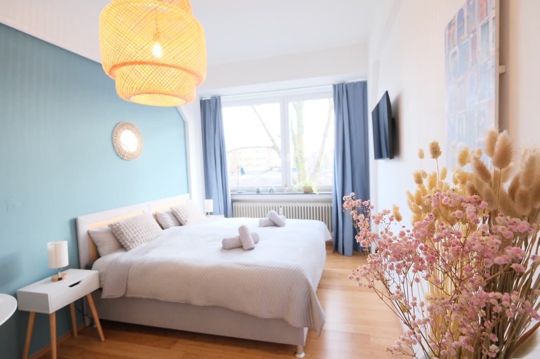 Schlafzimmer mit hellblauer Wand, Rattanleuchte und Trockenblumen
