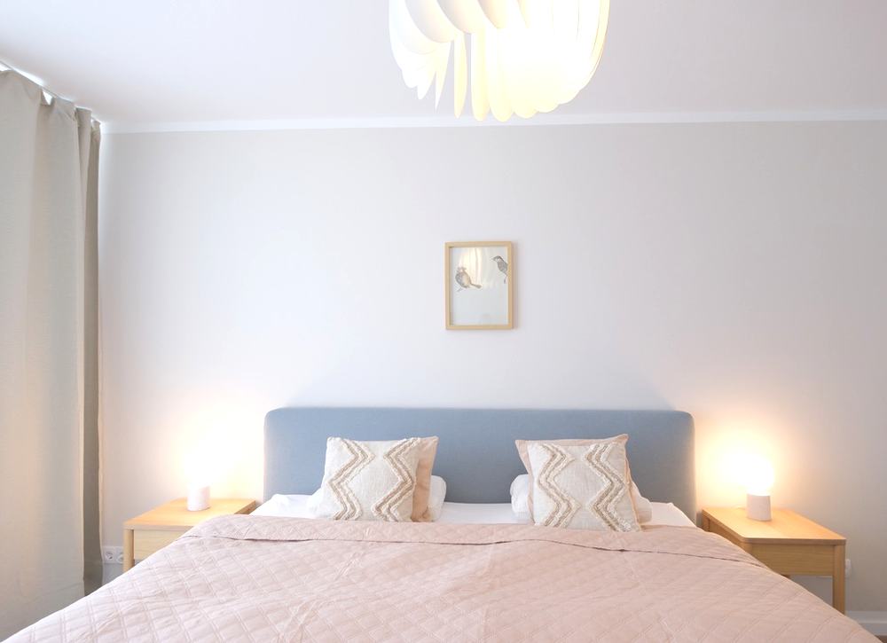 Schlafzimmer mit Polsterbett und rosé Tagesdecke, frontal