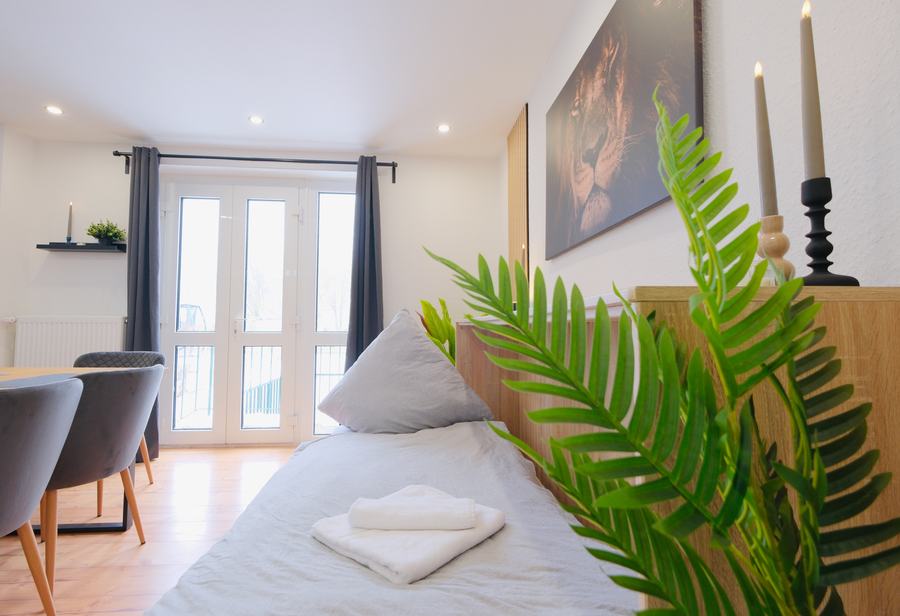Bett mit Farn-Deko und Blick in den Essbereich
